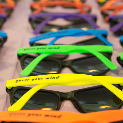 An array of multicolored sunglasses with the phrase "Queer Your Mind" on the temple